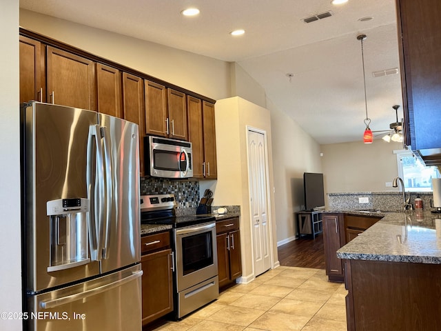 kitchen featuring vaulted ceiling, appliances with stainless steel finishes, pendant lighting, sink, and dark stone counters