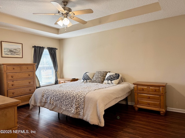 bedroom with dark wood-type flooring, ceiling fan, a tray ceiling, and a textured ceiling