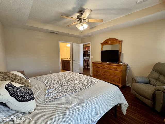 bedroom with connected bathroom, a tray ceiling, dark hardwood / wood-style floors, and ceiling fan