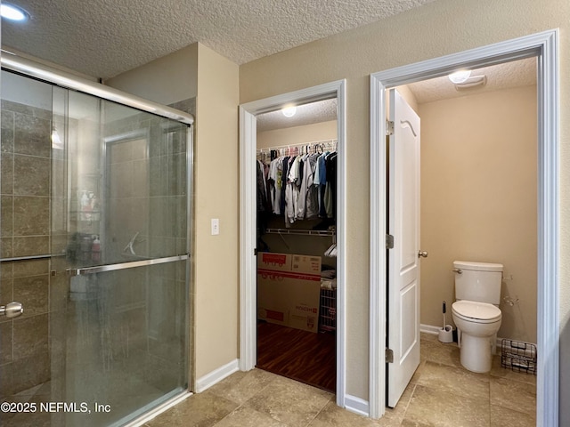 bathroom featuring a textured ceiling, a shower with shower door, and toilet