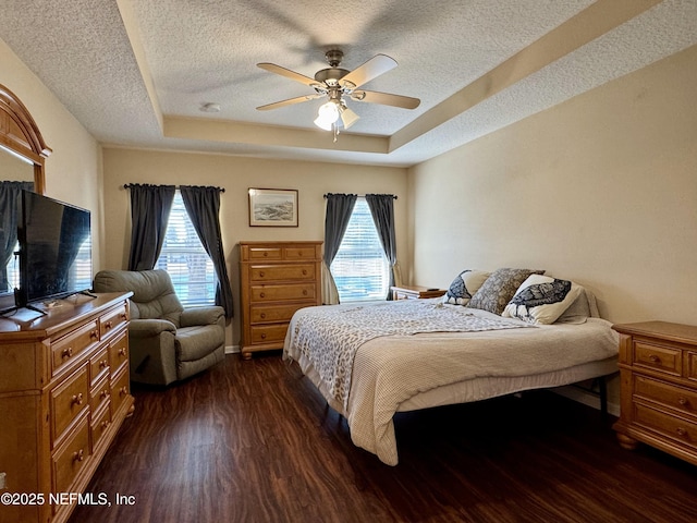 bedroom with ceiling fan, dark hardwood / wood-style floors, a raised ceiling, and multiple windows