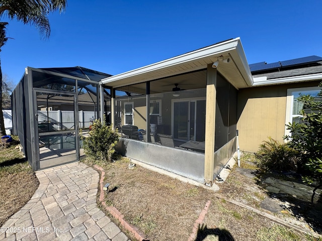 rear view of house featuring solar panels, glass enclosure, ceiling fan, a fenced in pool, and a sunroom