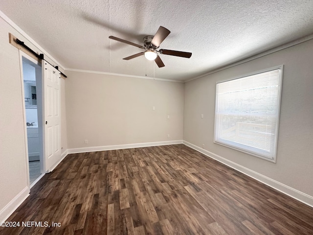 empty room with a textured ceiling, dark hardwood / wood-style floors, crown molding, and a barn door