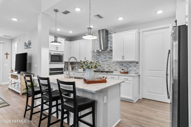 kitchen with wall chimney range hood, white cabinets, and appliances with stainless steel finishes