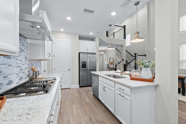 kitchen featuring a sink, visible vents, stainless steel appliances, light wood-type flooring, and wall chimney exhaust hood