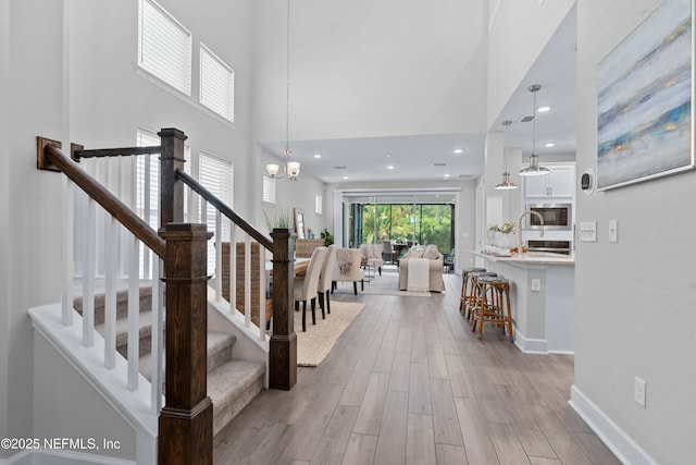 entrance foyer with wood finished floors, stairs, a chandelier, baseboards, and a towering ceiling