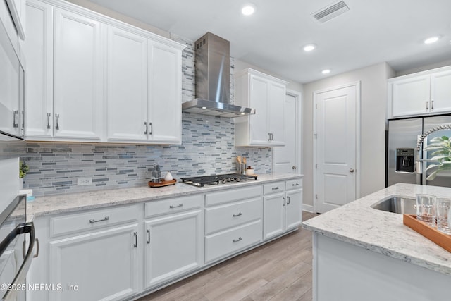 kitchen featuring stainless steel appliances, white cabinets, light wood finished floors, visible vents, and wall chimney exhaust hood