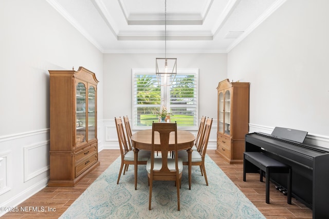 dining room featuring a tray ceiling, a wainscoted wall, crown molding, light wood finished floors, and a decorative wall