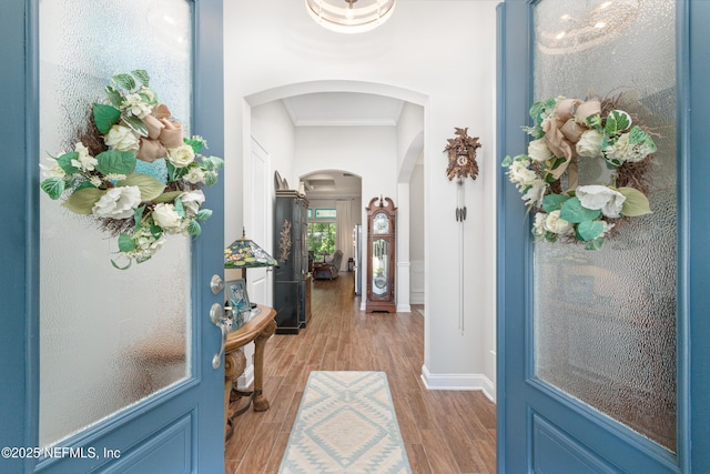 interior space featuring arched walkways, crown molding, and light wood-style flooring