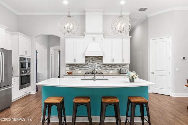 kitchen featuring appliances with stainless steel finishes, light countertops, a center island with sink, and hanging light fixtures