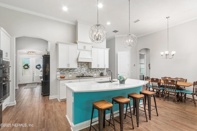 kitchen with arched walkways, light countertops, a kitchen island with sink, and white cabinets