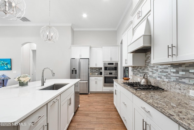 kitchen with white cabinets, ornamental molding, decorative light fixtures, stainless steel appliances, and a sink