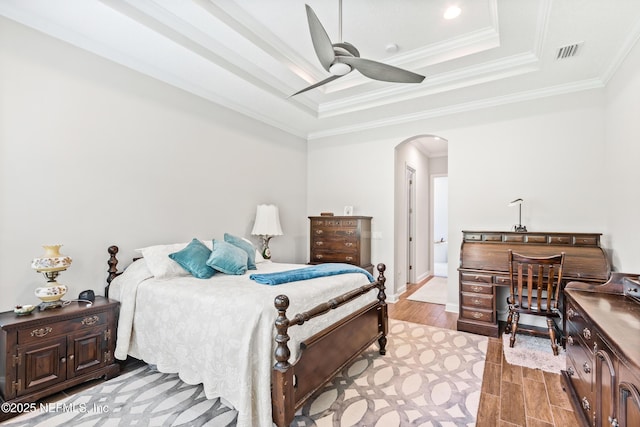 bedroom with visible vents, arched walkways, a tray ceiling, crown molding, and light wood-type flooring