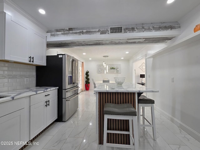 kitchen featuring stainless steel fridge, hanging light fixtures, light stone counters, white cabinets, and a kitchen bar