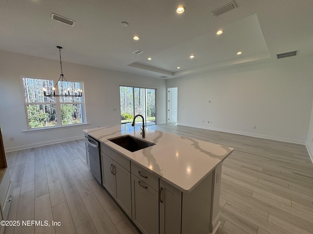 kitchen with a kitchen island with sink, gray cabinets, a raised ceiling, and dishwasher