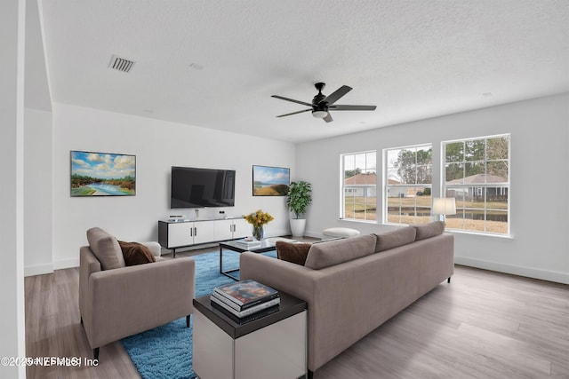 living room featuring ceiling fan, light hardwood / wood-style flooring, and a textured ceiling