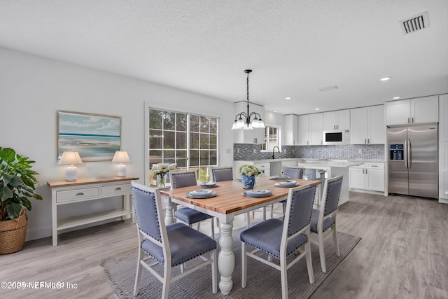 dining room featuring sink, light hardwood / wood-style floors, a textured ceiling, and a notable chandelier