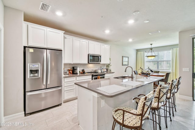 kitchen with an island with sink, sink, stainless steel appliances, and white cabinetry