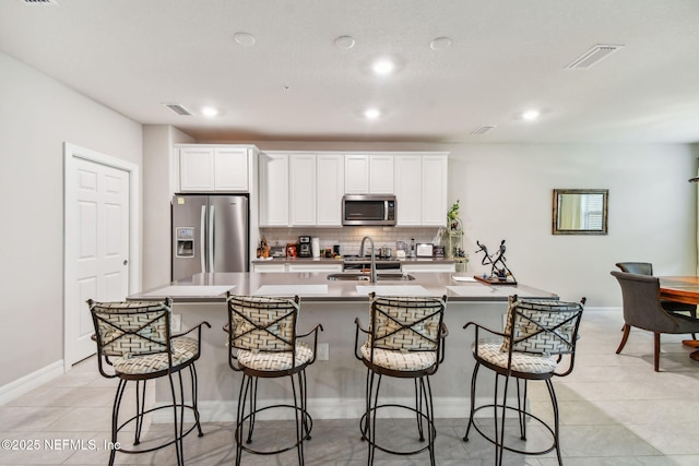 kitchen featuring light tile patterned floors, a kitchen bar, stainless steel appliances, white cabinets, and sink