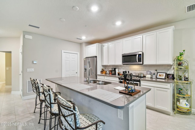 kitchen with white cabinets, sink, stainless steel appliances, and a center island with sink