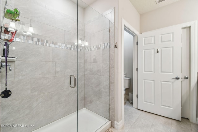 bathroom featuring toilet, tile patterned flooring, and a shower with shower door