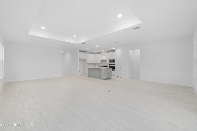 unfurnished living room featuring a raised ceiling and light hardwood / wood-style flooring