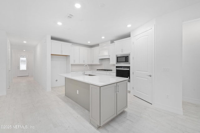 kitchen with white cabinetry, sink, black appliances, and an island with sink