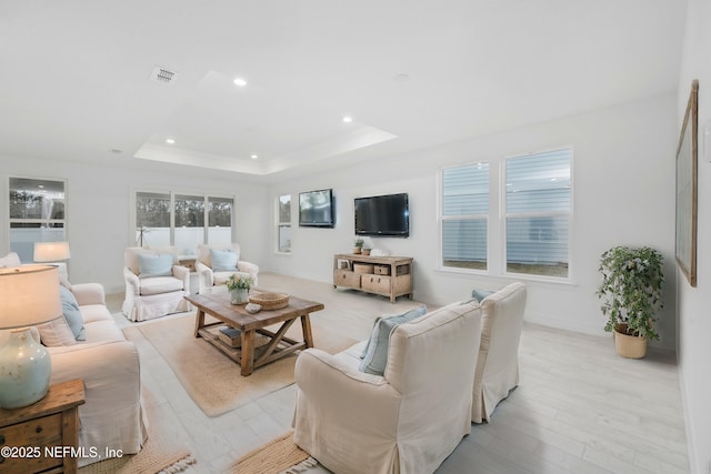 living room with a tray ceiling and light wood-type flooring