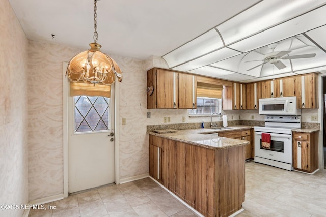 kitchen with ceiling fan with notable chandelier, pendant lighting, sink, kitchen peninsula, and white appliances