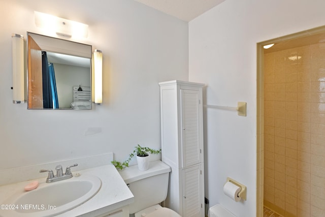 bathroom with toilet, tiled shower, and vanity