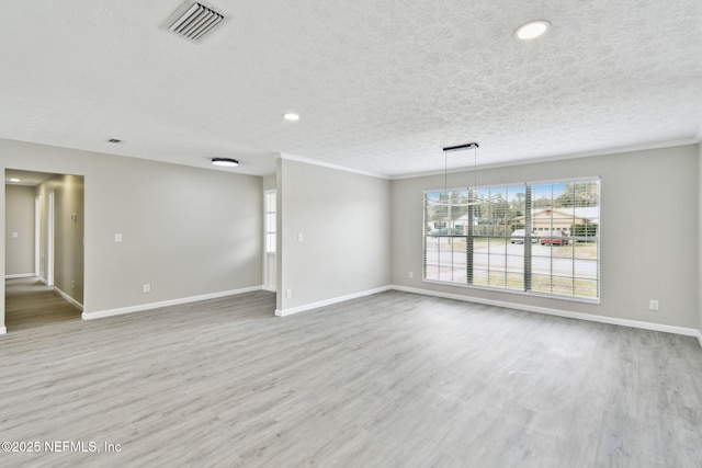 unfurnished living room featuring wood finished floors, visible vents, baseboards, a textured ceiling, and crown molding