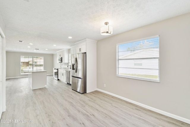 kitchen with a sink, white cabinets, light wood-style floors, appliances with stainless steel finishes, and a textured ceiling