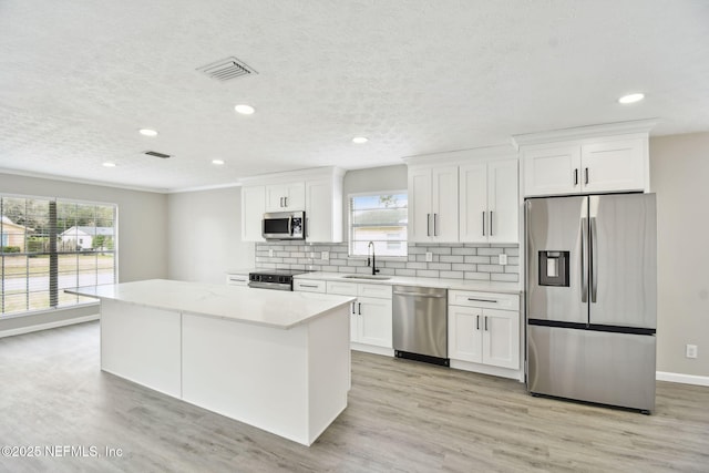 kitchen with visible vents, a kitchen island, a sink, appliances with stainless steel finishes, and tasteful backsplash