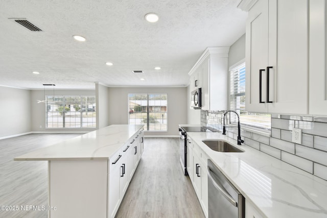 kitchen featuring light wood finished floors, visible vents, a kitchen island, appliances with stainless steel finishes, and a sink