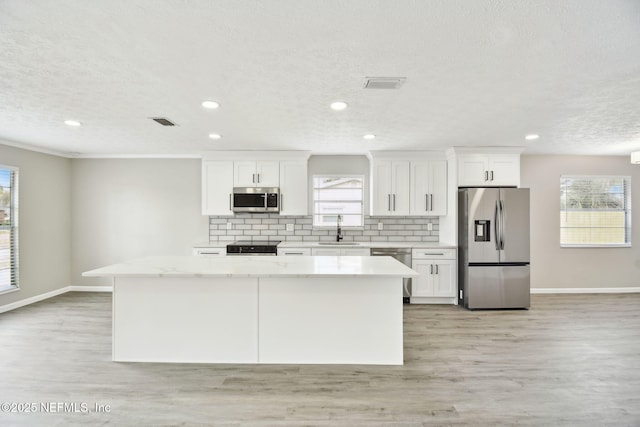 kitchen featuring visible vents, a sink, backsplash, a center island, and appliances with stainless steel finishes