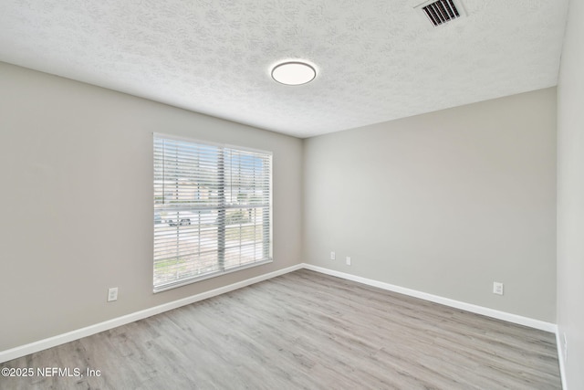 unfurnished room featuring a textured ceiling, wood finished floors, visible vents, and baseboards