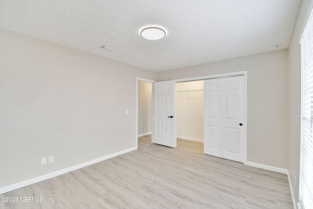 unfurnished bedroom with baseboards, light wood-type flooring, a closet, and a textured ceiling