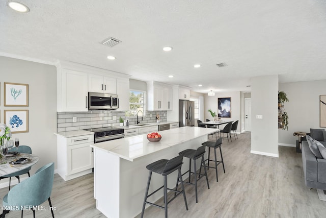 kitchen with a kitchen bar, a sink, a kitchen island, backsplash, and stainless steel appliances