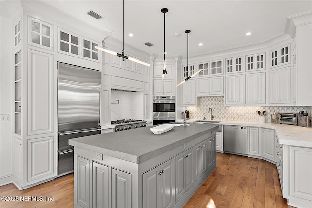 kitchen with decorative light fixtures, white cabinetry, stainless steel appliances, light hardwood / wood-style floors, and a center island with sink