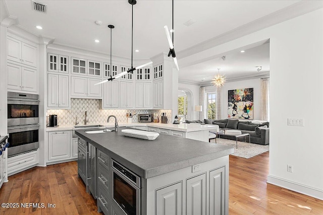 kitchen featuring an island with sink, stainless steel appliances, ornamental molding, pendant lighting, and white cabinets