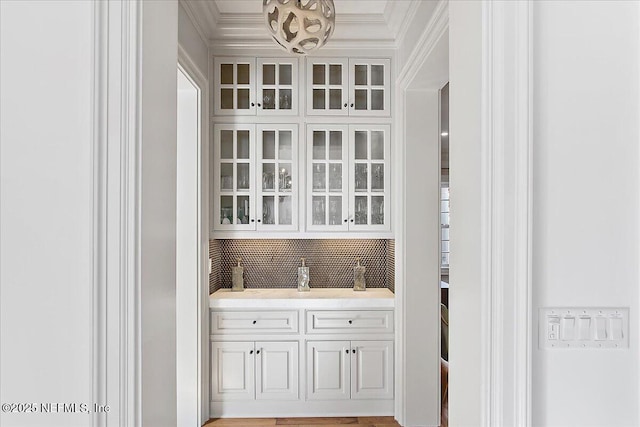 bar with white cabinets, backsplash, and crown molding