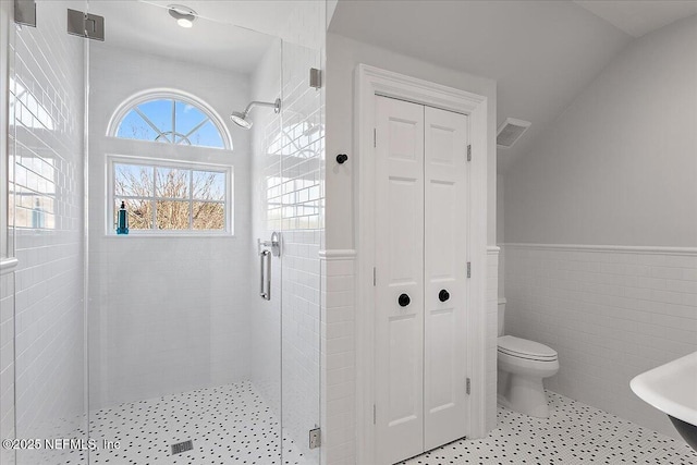 bathroom featuring toilet, tile walls, and a shower with door