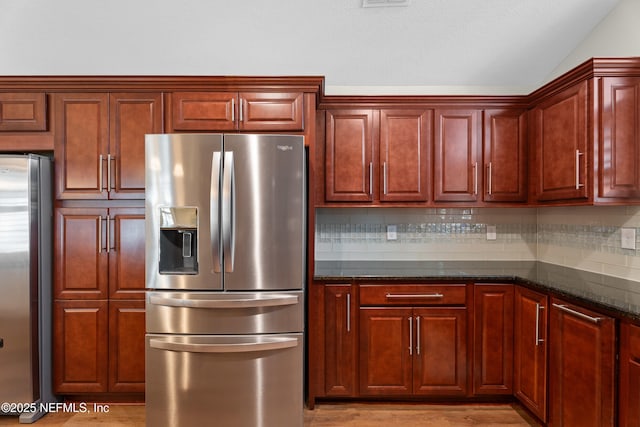 kitchen with lofted ceiling, stainless steel refrigerator, dark stone countertops, backsplash, and stainless steel refrigerator with ice dispenser