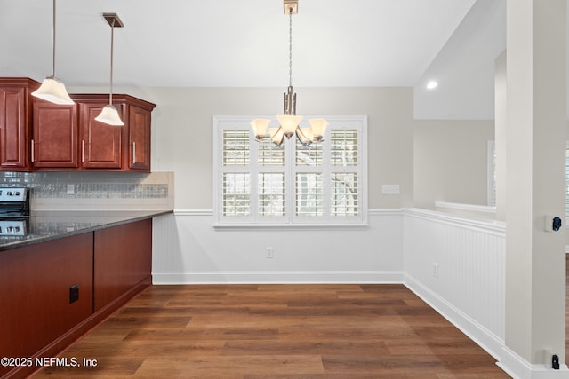 kitchen featuring dark wood-type flooring, a chandelier, hanging light fixtures, dark stone counters, and backsplash