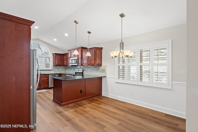 kitchen with appliances with stainless steel finishes, pendant lighting, lofted ceiling, light hardwood / wood-style floors, and kitchen peninsula