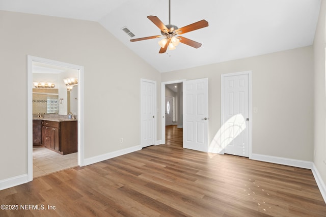 unfurnished bedroom featuring lofted ceiling, two closets, light wood-type flooring, and ensuite bath