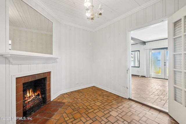 unfurnished living room with an inviting chandelier, ornamental molding, a tiled fireplace, and french doors