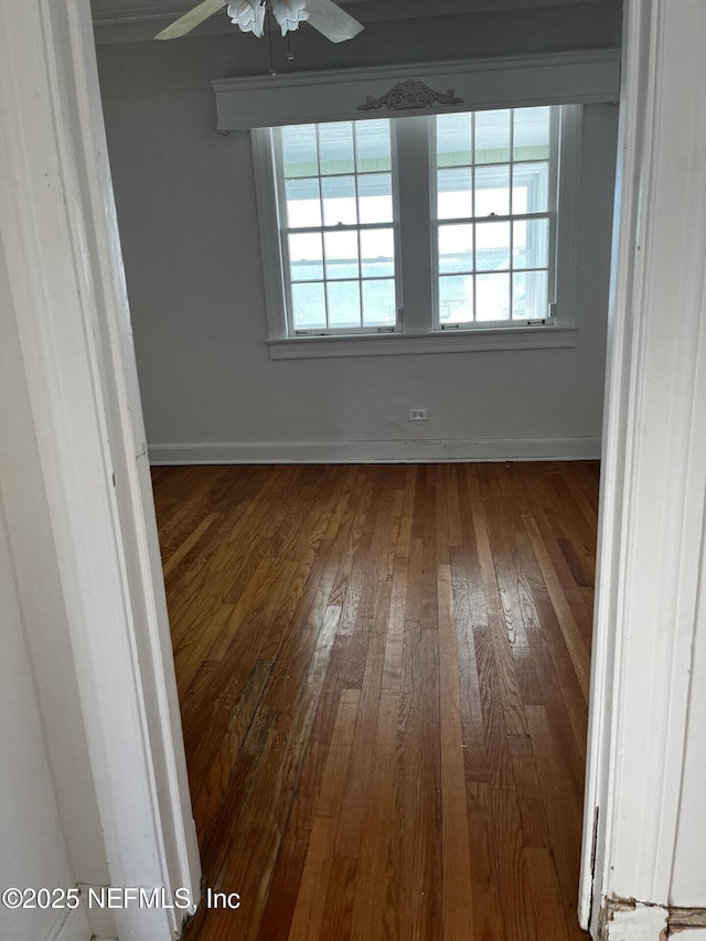 unfurnished room with baseboards, ceiling fan, dark wood-type flooring, and a healthy amount of sunlight