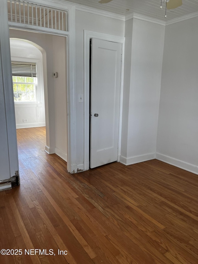 empty room with arched walkways, baseboards, crown molding, and hardwood / wood-style floors