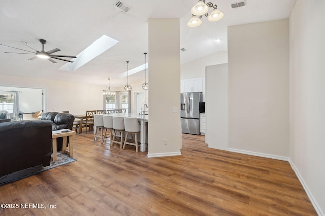 living room with hardwood / wood-style flooring, vaulted ceiling with skylight, sink, and ceiling fan with notable chandelier